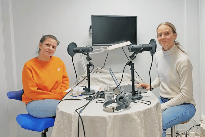 2 damer i podcast studio. begge ser rett i kameraet