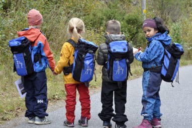 4 barn med ryggen til på vei til skolen. Foto.